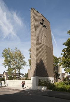 people are walking around in front of a tall building with a cross on it's side