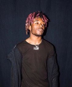 a man with pink dreadlocks standing in front of a black background