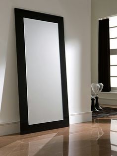 a large mirror sitting on the floor in front of a window next to a vase