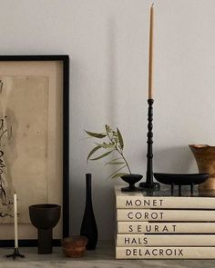 a stack of books sitting on top of a table next to a vase and candle