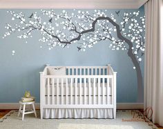 a baby's room with a tree painted on the wall and a white crib