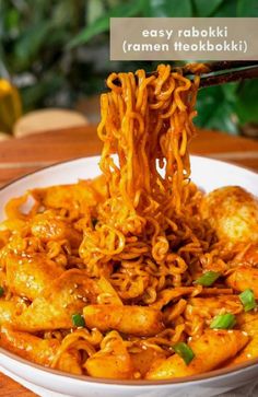 the noodles are being eaten with chopsticks in a white bowl on top of a wooden table