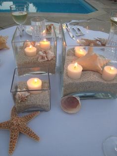 candles are placed in glass containers with seashells and starfish on the table