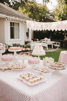 a table topped with lots of cupcakes next to a white and pink cake