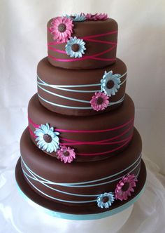 a three tiered chocolate cake with pink, blue and white flowers on the top