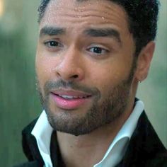 a close up of a person wearing a black jacket and white shirt with his hair pulled back