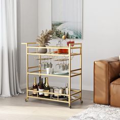 a bar cart with bottles and glasses on it in front of a couch next to a window