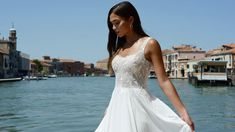 a beautiful woman in a white dress standing on the edge of a body of water