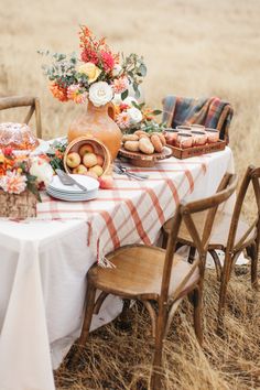 a table set with food and flowers on it in the middle of an open field