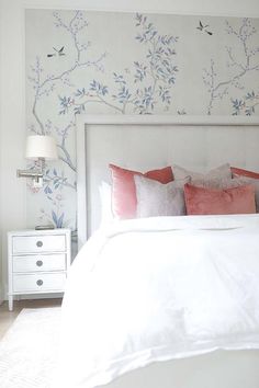 a white bed topped with pillows next to a wallpaper covered in pink and blue flowers