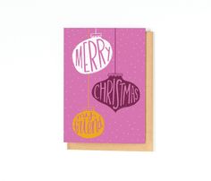 a pink christmas card with two ornaments hanging from it's string and the words merry