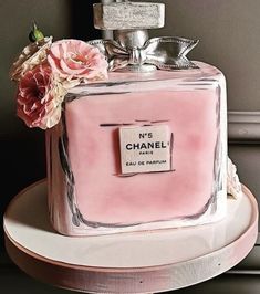 a chanel bottle cake with pink flowers on the top and silver trimmings