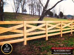 a wooden fence in the middle of a grassy area with trees and grass on both sides