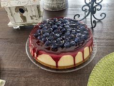 a cheesecake covered in blueberries on top of a glass cake plate next to a birdhouse