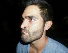 a close up of a man with a beard and blue shirt looking off into the distance