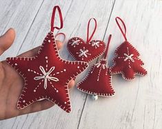 three red christmas ornaments hanging from strings on a white wooden table with a person's hand holding one ornament