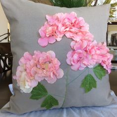 a pillow with pink flowers on it sitting on a table next to a potted plant