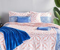 an orange and blue comforter set on a bed next to a potted plant