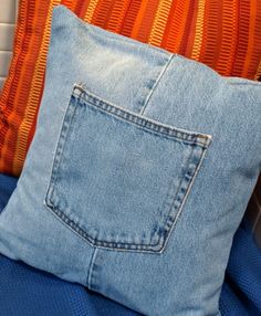 a blue jean pillow sitting on top of a bed next to an orange striped pillow