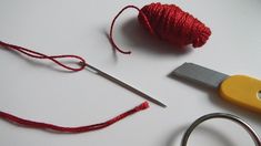 a pair of scissors, thread and needle on a white surface with red yarn next to it