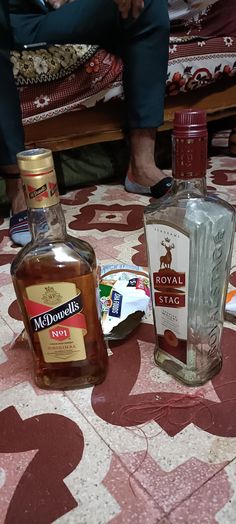 two bottles of alcohol sitting on top of a table next to a person's feet