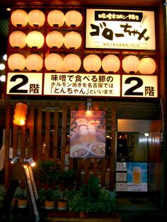 the outside of a restaurant with signs and lights on it's front wall,