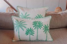 two pillows with green palm trees on them sitting on a couch in a living room