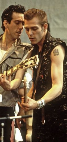 two men standing next to each other holding guitars