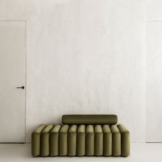 a green couch sitting in front of a white wall next to an open door on the floor