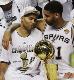 two basketball players sitting next to each other with their arms around one another and the trophy in front of them