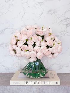 a vase filled with pink flowers sitting on top of a book next to a marble wall