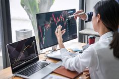 a woman is looking at her computer screen and pointing to the stock chart on it