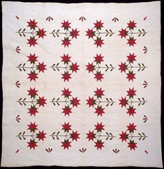 a white quilt with red and green flowers on the front, along with an arrow design