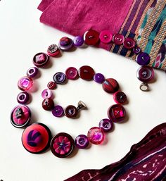 a bunch of buttons that are laying on a white surface next to a purple scarf