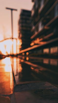 the sun is setting behind some buildings and street lights in front of an empty sidewalk