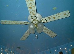 a ceiling fan with stars on it in a room that is blue and has white walls