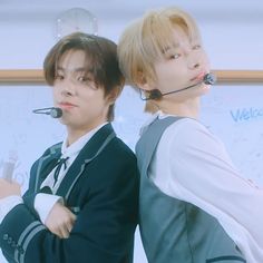 two young men with headsets on standing next to each other in front of a whiteboard