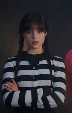 a woman with her arms crossed standing in front of a black and white striped shirt