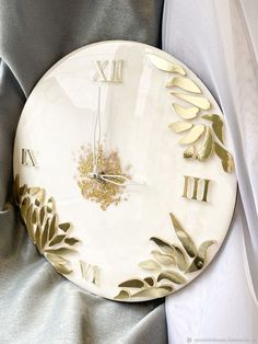 a white and gold clock with roman numerals sitting on a gray fabric background