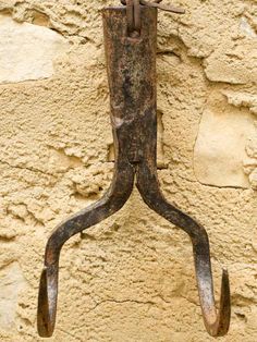 an old rusted metal hook hanging on a wall with nails sticking out of it