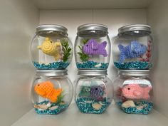 four fish in small glass jars filled with blue and yellow glittery water, one is goldfish