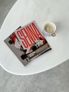 a magazine sitting on top of a white table next to a cup of coffee in front of it