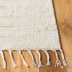 a white rug with tassels laying on a wooden floor