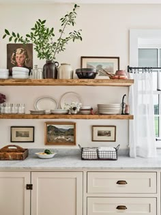 a kitchen with white cabinets and shelves filled with plates, bowls and utensils