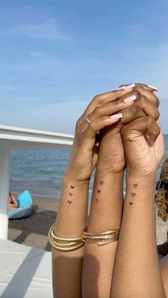 two women with matching tattoos on their arms near the ocean and beach, one holding her hands up to her head