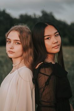 two women standing next to each other in front of a field with grass and trees