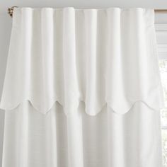 a white curtain with ruffles hanging from it's rod ends in front of a window