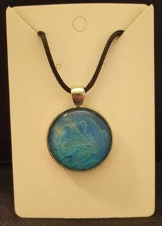 a necklace with a blue and green pendant on it's leather cord in front of a white box