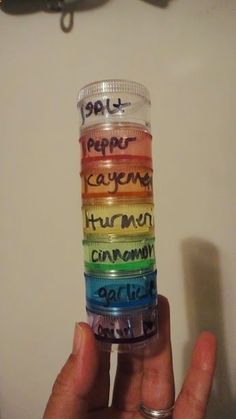 a person holding up a stack of small jars filled with different colored writing on them