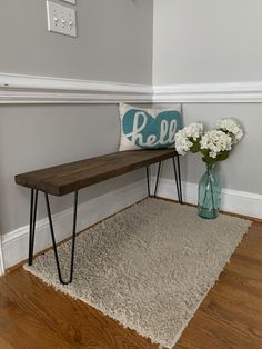 a wooden bench sitting next to a vase with white flowers on it and a pillow